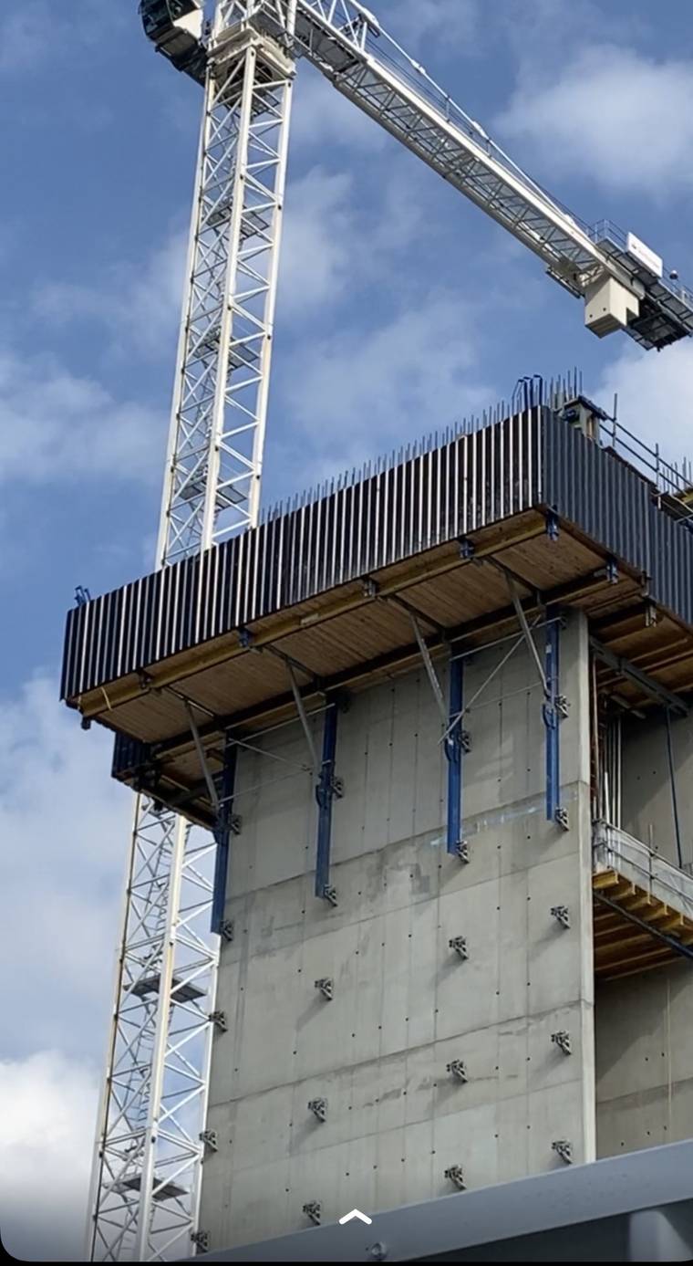 Climbing formwork platform and wall panels cantilevered from an in-situ concrete core, with a tower crane above.