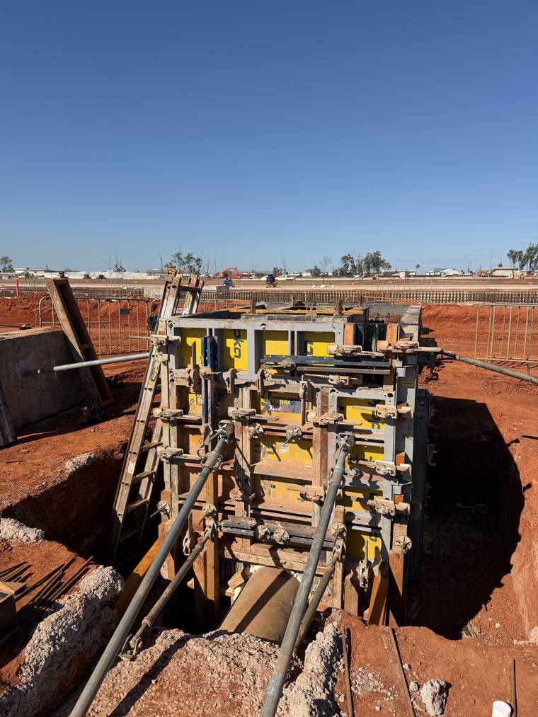 Ganged formwork panels propped and aligned within a deep excavation under a clear sky.