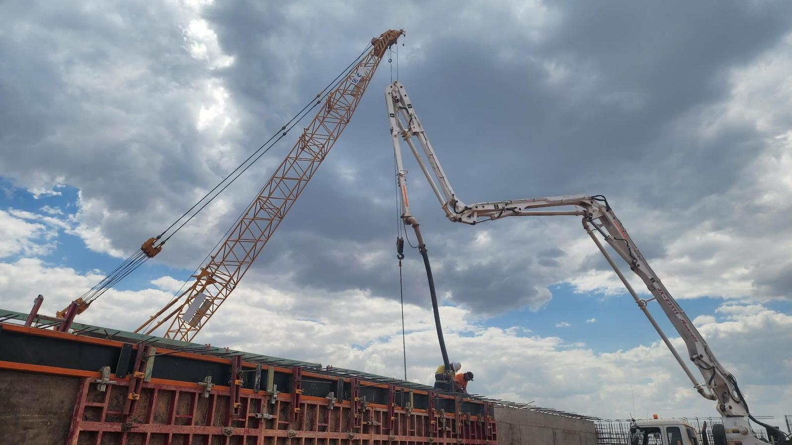 Concrete pump boom and crawler crane over a wall pour, with operatives working from the top of the wall formwork.